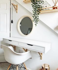 there is a white desk and chair under the stairs in this room, with a round mirror above it