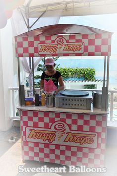 a woman standing behind a food cart selling hot dogs