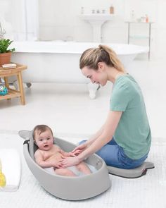 a woman sitting on the floor with a baby in a bathtub next to it