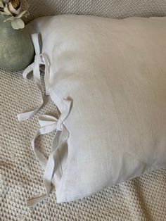 a white pillow on a bed with a flower in a vase sitting next to it