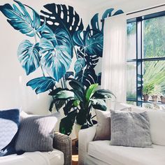 a living room filled with white couches and large green leaves on the wall behind them