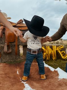 a small child wearing a cowboy hat holding the hand of an adult's hand