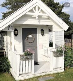 a small white shed with flowers on the porch