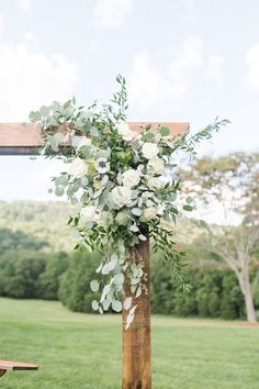 a wooden cross with white flowers and greenery hanging from it's sides in the grass