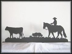 the silhouettes of two people on horses and cows are shown in front of a white wall