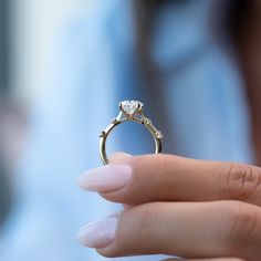 a woman's hand holding an engagement ring with a heart shaped diamond on it