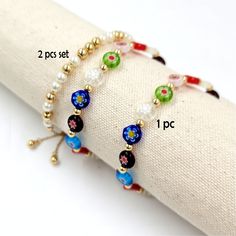 three bracelets with different colored beads are on a white cloth roll and one is gold, the other is blue