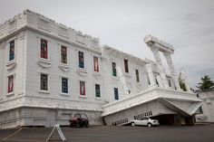 a large white building with red and green shutters on it's sides, next to a parking lot