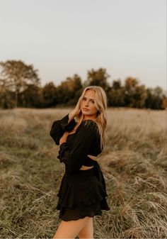 a woman standing in the middle of a field with her hands on her hips and looking at the camera