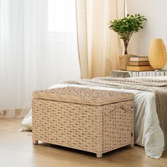 a wicker bed with white linens and a plant on the end table next to it