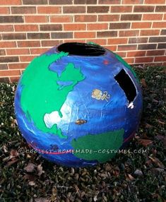 a blue and green painted globe sitting in the grass next to a brick wall,