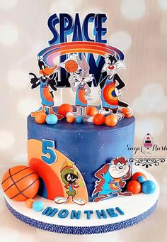 a birthday cake decorated with cartoon characters and basketballs is shown on a tablecloth