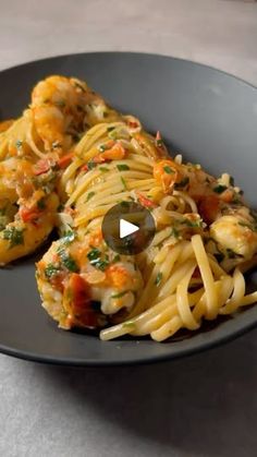 a black plate topped with pasta covered in sauce and shrimp next to green olives