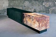 a marble bench sitting in front of a stone wall and cement floored room with concrete walls