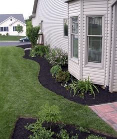 a house with grass and flowers in the front yard, next to a brick walkway