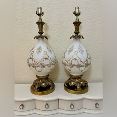 two white and gold vases sitting on top of a shelf