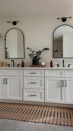 a bathroom with double sinks and two mirrors on the wall, along with a rug in front of it