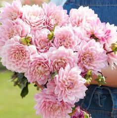 a woman holding a bouquet of pink flowers in her hands and wearing an overalls