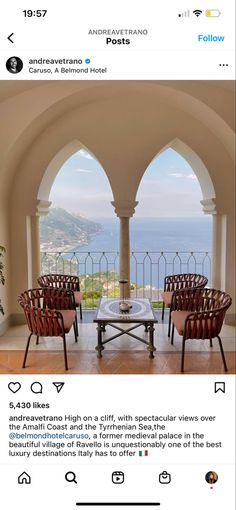 the inside of a house with an arched window and chairs in front of it, looking out onto the ocean