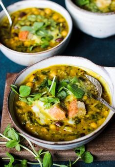 two bowls filled with soup on top of a wooden cutting board and garnished with fresh herbs