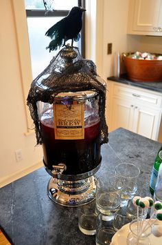 a black bird sitting on top of a jar filled with liquid next to two glasses