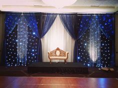 a stage set up for a party with blue lights and drapes on the walls