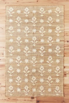 a beige rug with white flowers and leaves on top of wooden flooring next to a wall