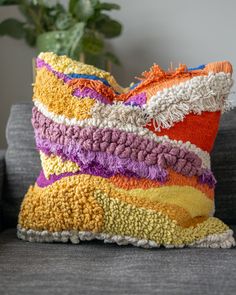 a multicolored pillow sitting on top of a couch next to a potted plant