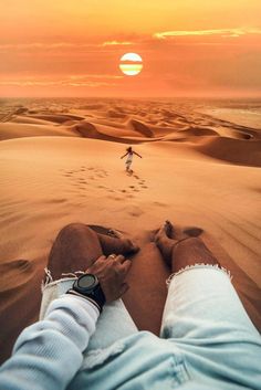 the person is laying down in the sand with their feet up on the ground while the sun sets