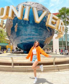 a woman posing in front of the universal studios sign with her arms outstretched and legs spread out