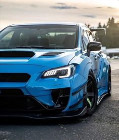 the front end of a blue subarunt car parked in a parking lot at sunset