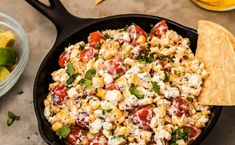 a skillet filled with corn salad and tortilla chips next to a bowl of guacamole