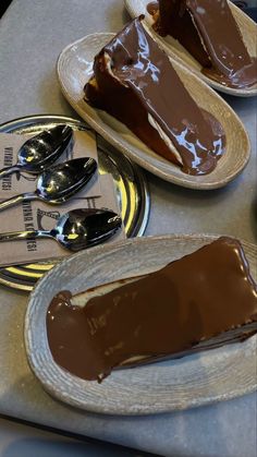 two plates with slices of chocolate cake on them and spoons next to each other