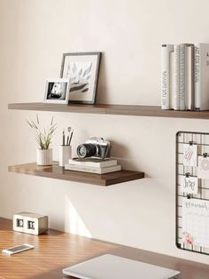 a desk with some books and pictures on the shelves next to a laptop, phone, camera and other items