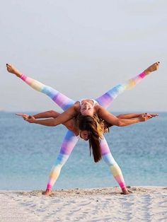 two girls doing yoga on the beach with their arms in the air and one girl upside down