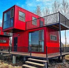 two red shipping containers sitting next to each other on top of a wooden deck with stairs leading up to the second floor