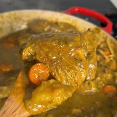 a wooden spoon full of stew with carrots and meat in it on the stove