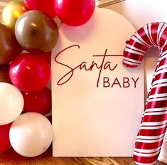 a santa baby sign next to balloons and a candy cane