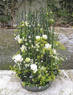 a vase filled with white flowers sitting on top of a stone wall next to plants