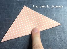 a hand is pointing at a piece of paper with white dots on it and the tip of an origami triangle