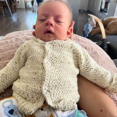 a baby laying on top of a woman's lap wearing a sweater and diaper