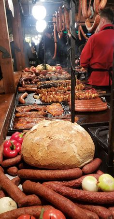 many sausages and bread are on display in a kitchen with people standing behind them