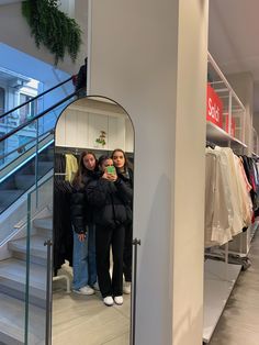 two women standing in front of a mirror looking at their cell phones and taking a selfie