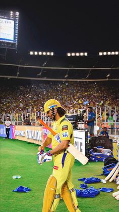 a man walking across a field with a bat in his hand and people watching from the stands behind him