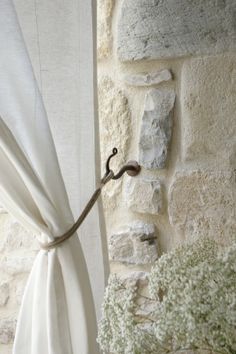 a white curtain hanging on the side of a stone wall next to a potted plant