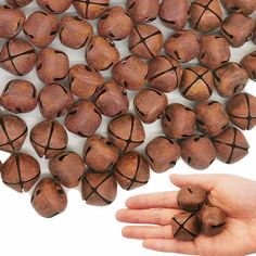 a hand holding a bunch of wooden bells on top of a white table next to a pile of wood beads