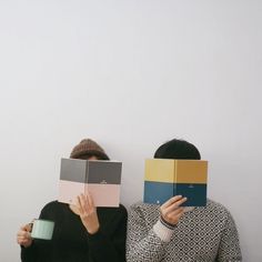 two people sitting on the floor with books covering their faces and holding coffee mugs