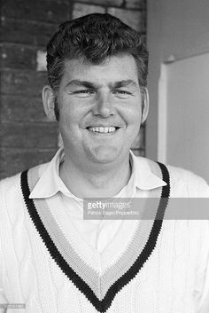 a black and white photo of a man wearing a sweater smiling at the camera with his hands in his pockets