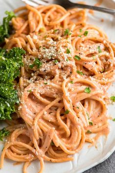 a white plate topped with pasta and broccoli next to a fork on a table