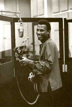 a man standing in front of a microphone holding a guitar and smiling at the camera